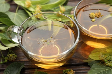 Photo of Fresh linden tea in cups and flowers on wooden table, closeup