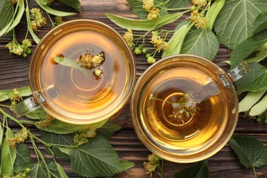 Photo of Fresh linden tea in cups and flowers on wooden table, flat lay