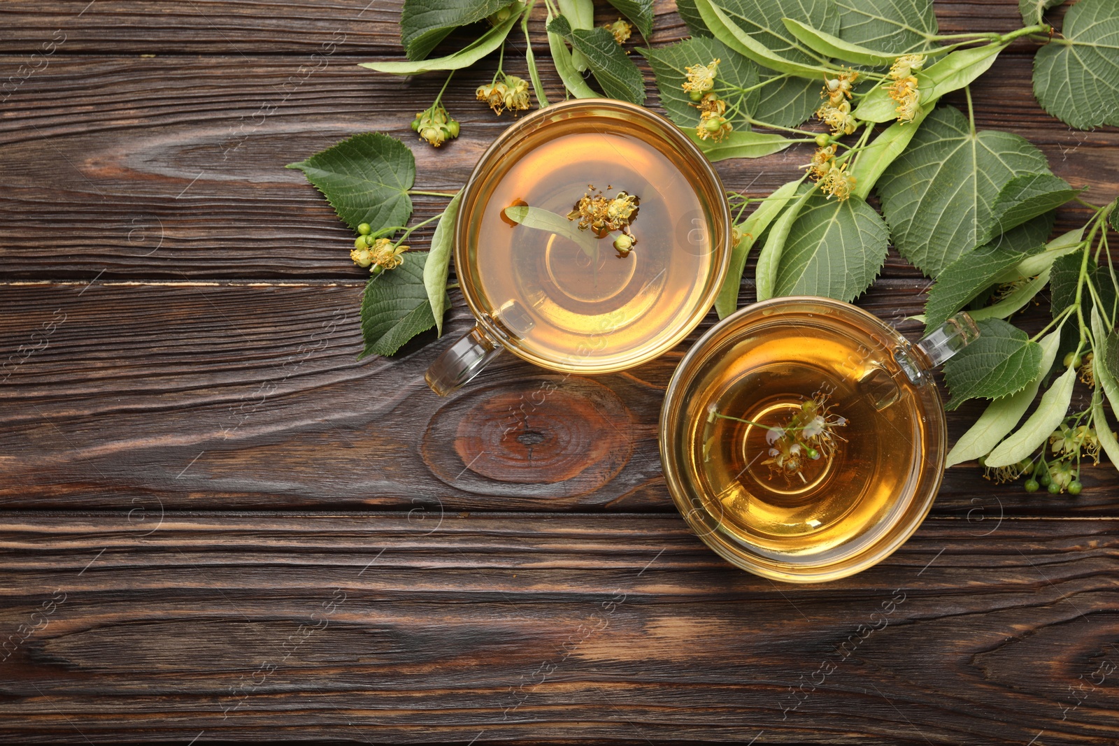 Fresh linden tea in cups and flowers on wooden table, flat lay. Space for text Photo of Fresh linden tea in cups and flowers on wooden table, flat lay. Space for text