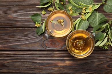Photo of Fresh linden tea in cups and flowers on wooden table, flat lay. Space for text