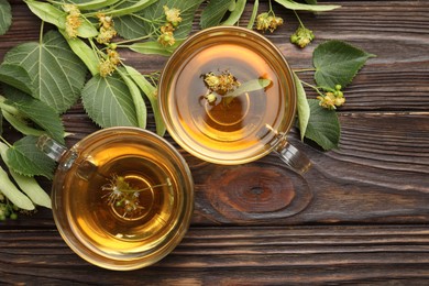 Photo of Fresh linden tea in cups and flowers on wooden table, flat lay. Space for text