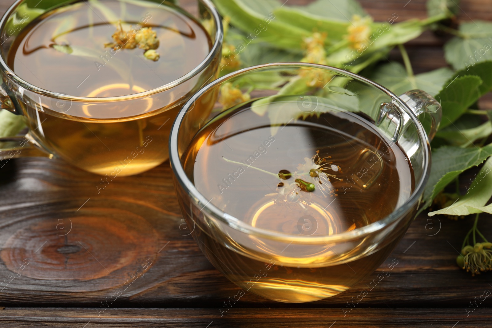 Fresh linden tea in cups and flowers on wooden table, closeup Photo of Fresh linden tea in cups and flowers on wooden table, closeup