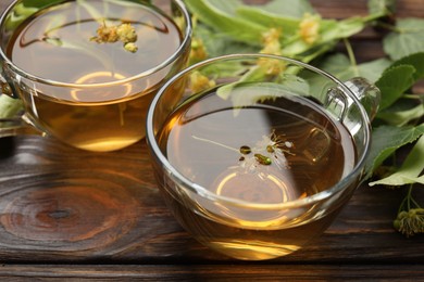 Photo of Fresh linden tea in cups and flowers on wooden table, closeup