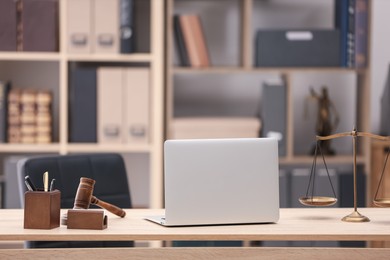 Photo of Judge's gavel, scales, laptop and stationery on wooden table in office