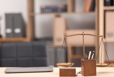 Photo of Judge's gavel, scales, laptop and stationery on wooden table in office