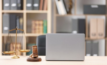 Photo of Judge's gavel, scales and laptop on wooden table in office