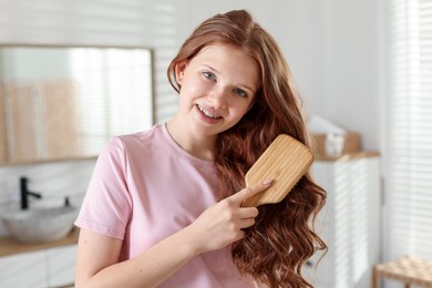 Photo of Smiling teenage girl brushing her shiny hair at home
