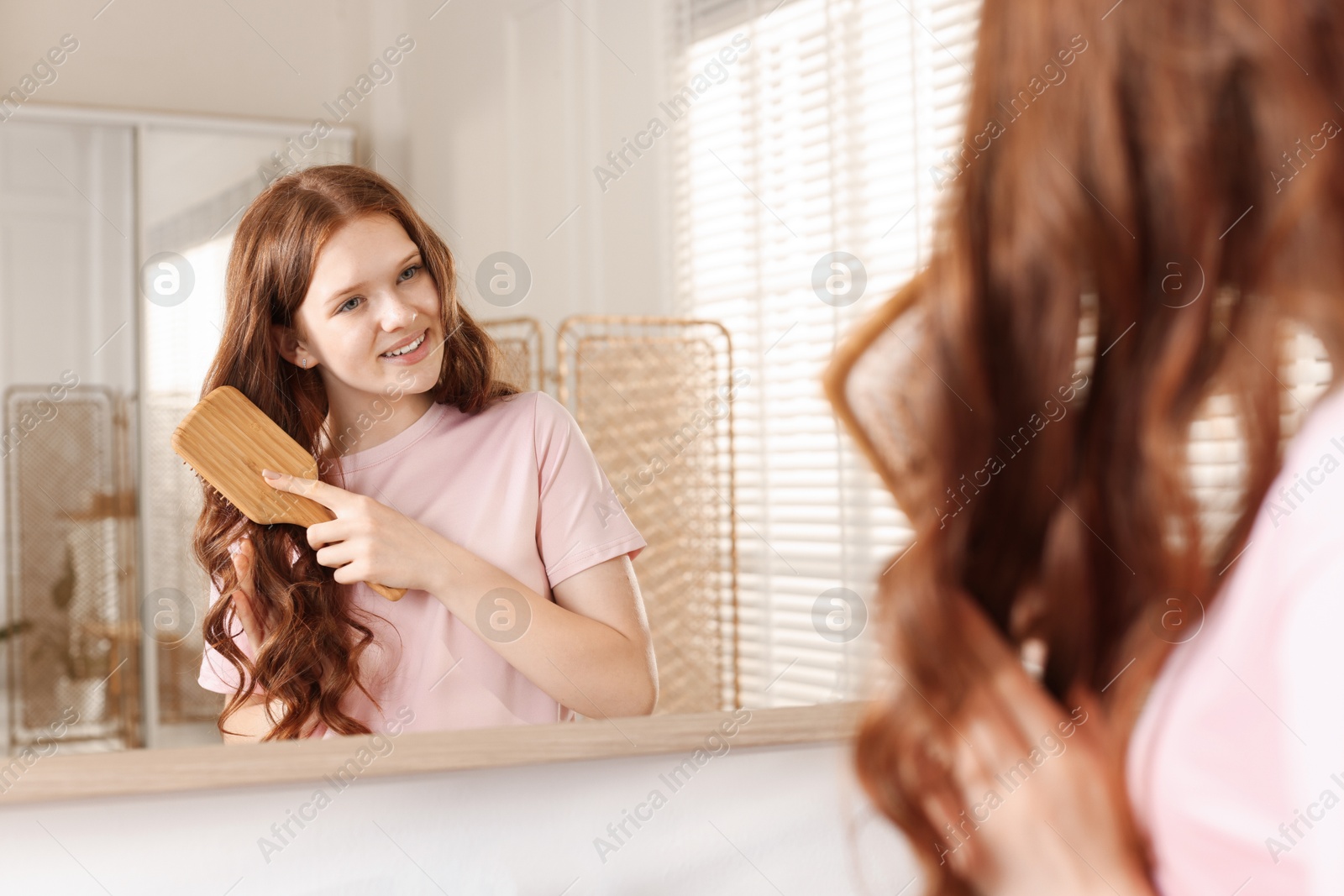 Smiling teenage girl brushing her shiny hair near mirror at home Photo of Smiling teenage girl brushing her shiny hair near mirror at home