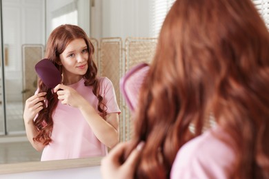 Photo of Teenage girl brushing her shiny hair near mirror at home