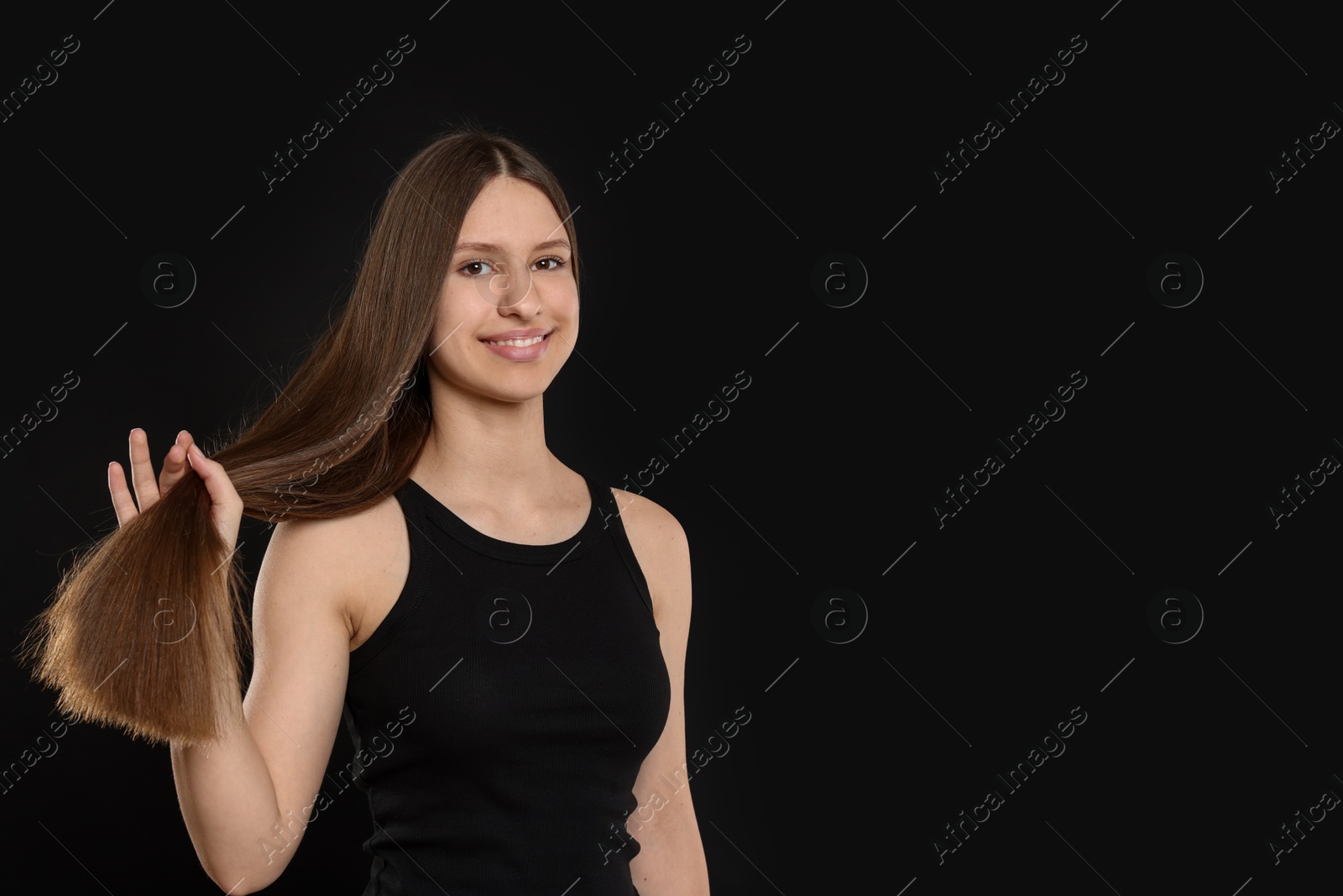 Smiling teenage girl with healthy long hair on black background. Space for text Photo of Smiling teenage girl with healthy long hair on black background. Space for text