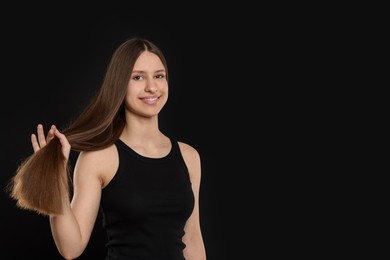 Photo of Smiling teenage girl with healthy long hair on black background. Space for text