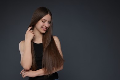 Photo of Smiling teenage girl with healthy long hair on dark grey background. Space for text