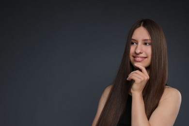Photo of Smiling teenage girl with healthy long hair on dark grey background. Space for text