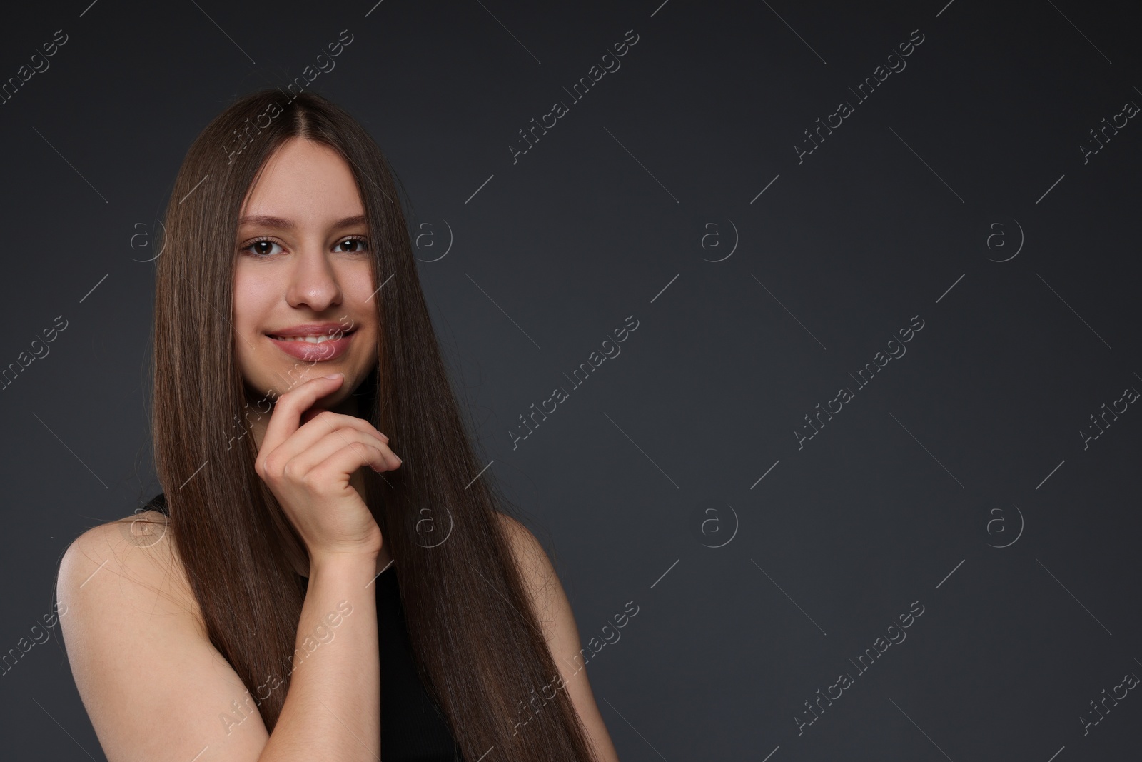 Portrait of smiling teenage girl with healthy long hair on dark grey background. Space for text Photo of Portrait of smiling teenage girl with healthy long hair on dark grey background. Space for text