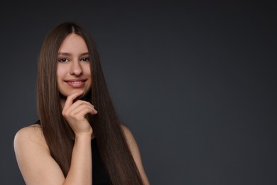Photo of Portrait of smiling teenage girl with healthy long hair on dark grey background. Space for text