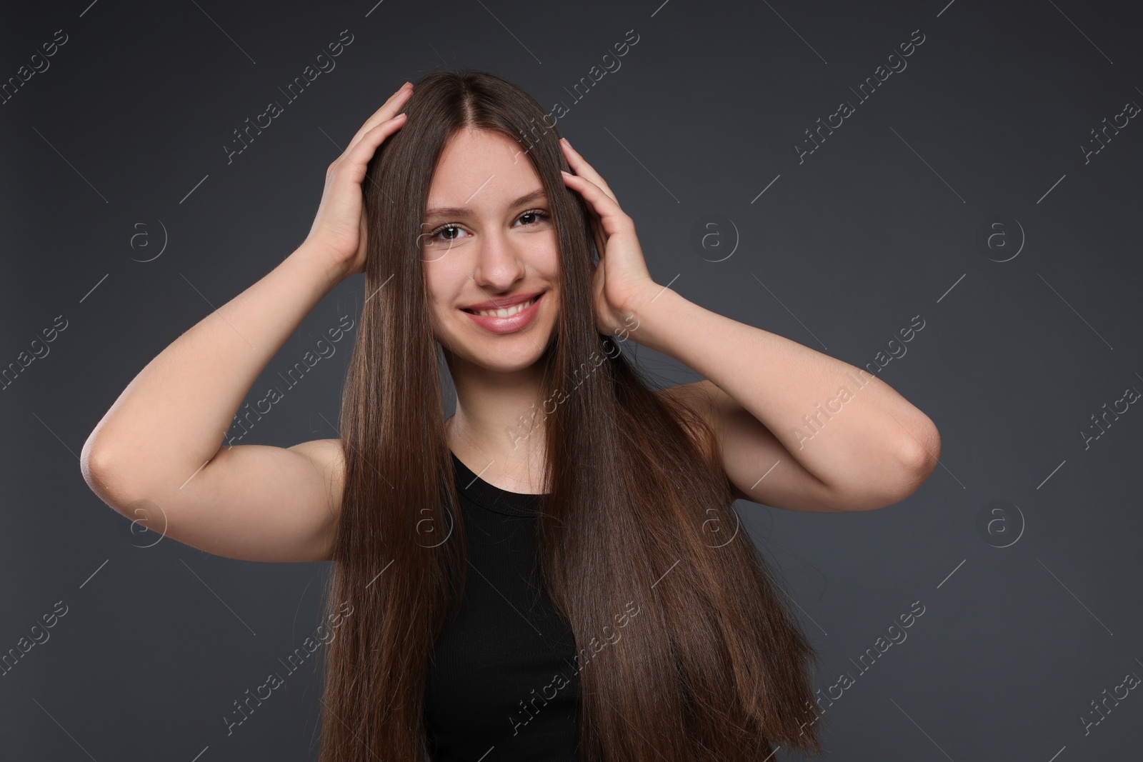 Portrait of smiling teenage girl with healthy long hair on dark grey background Photo of Portrait of smiling teenage girl with healthy long hair on dark grey background