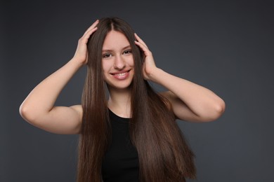 Photo of Portrait of smiling teenage girl with healthy long hair on dark grey background
