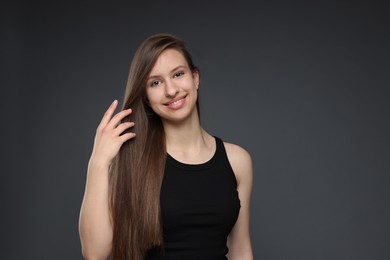 Photo of Portrait of smiling teenage girl with healthy long hair on dark grey background