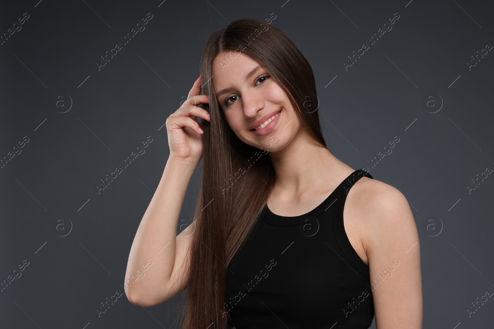 Portrait of smiling teenage girl with healthy long hair on dark grey background Photo of Portrait of smiling teenage girl with healthy long hair on dark grey background