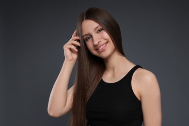 Photo of Portrait of smiling teenage girl with healthy long hair on dark grey background