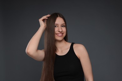 Photo of Portrait of smiling teenage girl with healthy long hair on dark grey background