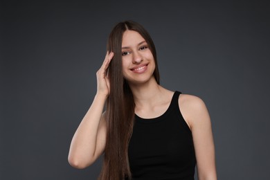Photo of Portrait of smiling teenage girl with healthy long hair on dark grey background