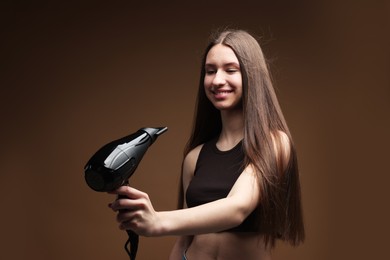 Photo of Smiling teenage girl with hair dryer on brown background
