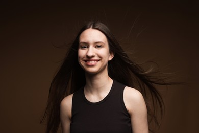 Photo of Portrait of smiling teenage girl with healthy long hair on brown background