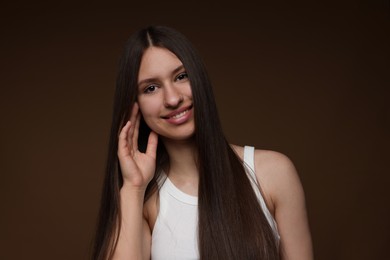 Photo of Portrait of smiling teenage girl with healthy long hair on brown background