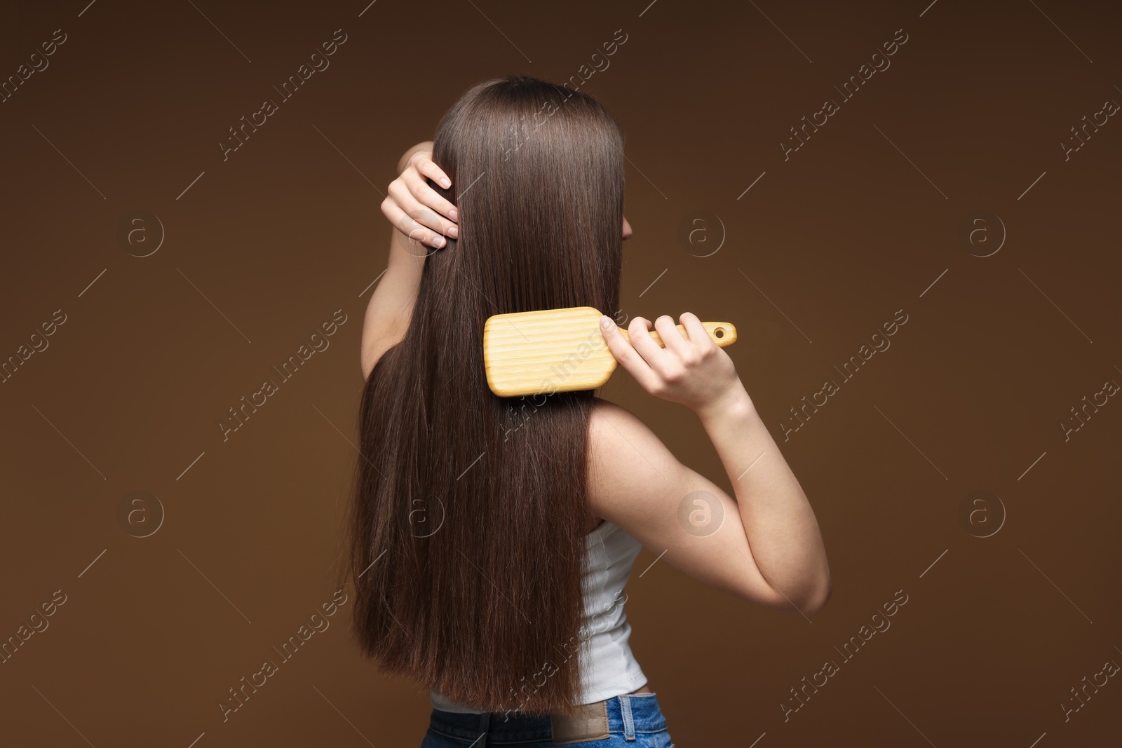 Photo of Teenage girl brushing her healthy long hair on brown background