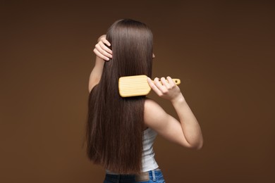 Photo of Teenage girl brushing her healthy long hair on brown background