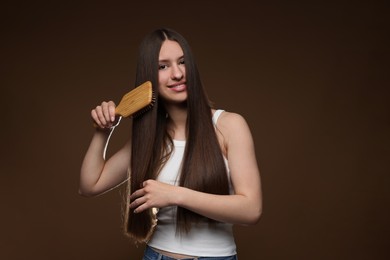 Photo of Smiling teenage girl brushing her healthy long hair on brown background