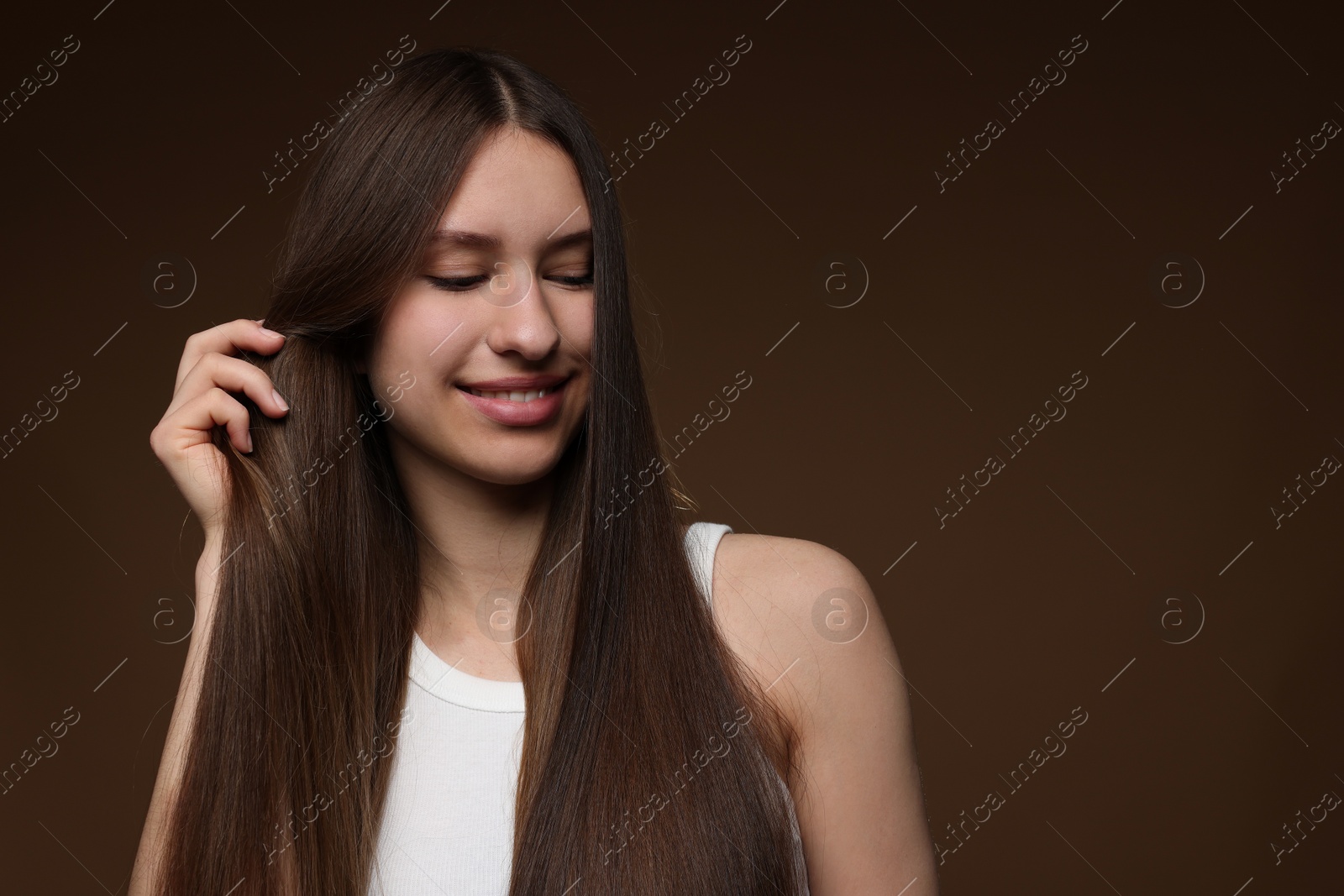 Smiling teenage girl with healthy long hair on brown background. Space for text Photo of Smiling teenage girl with healthy long hair on brown background. Space for text