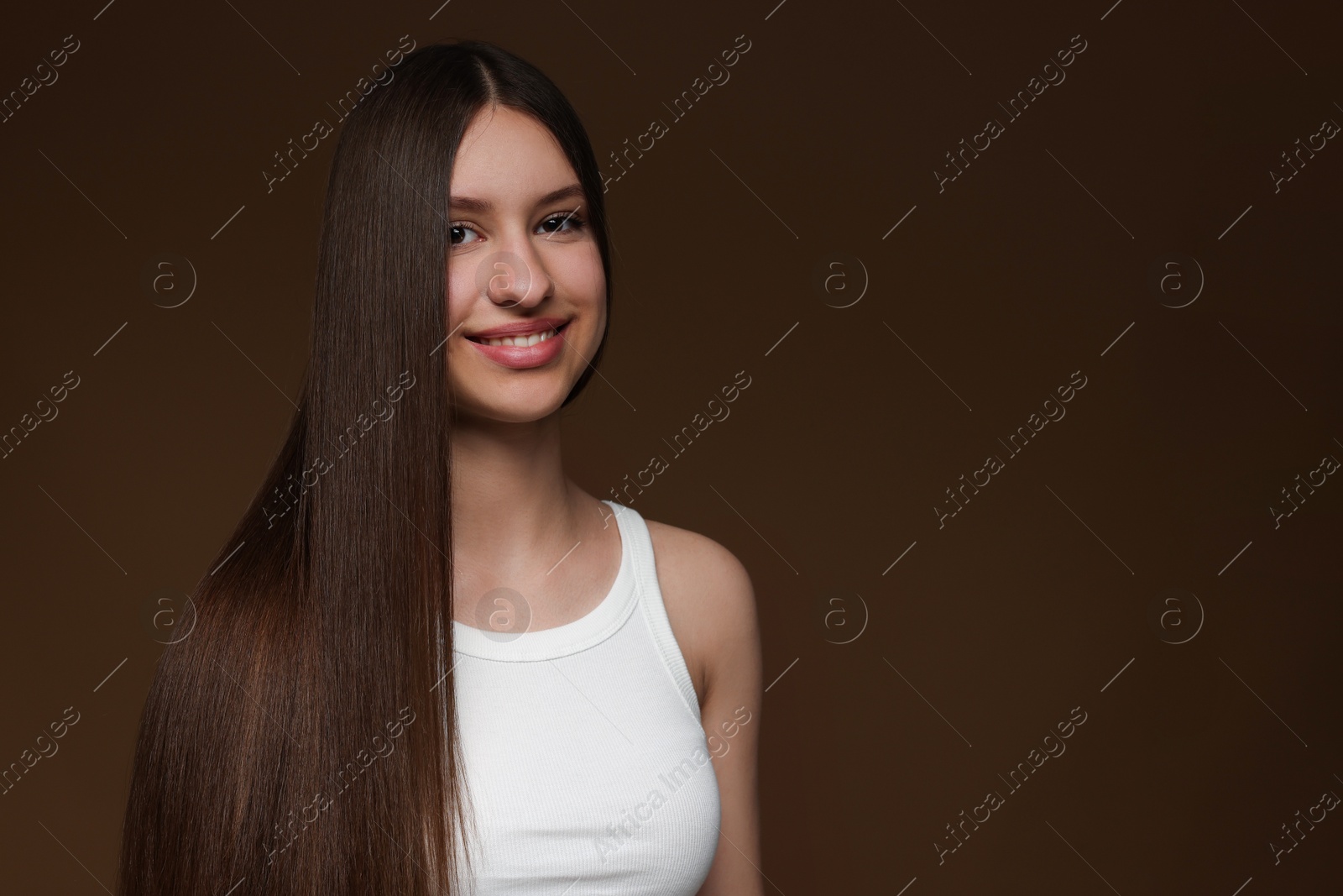 Portrait of smiling teenage girl with healthy long hair on brown background. Space for text Photo of Portrait of smiling teenage girl with healthy long hair on brown background. Space for text