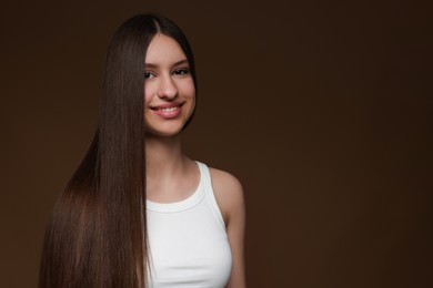Photo of Portrait of smiling teenage girl with healthy long hair on brown background. Space for text