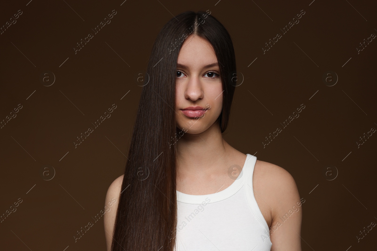 Portrait of beautiful teenage girl with healthy long hair on brown background Photo of Portrait of beautiful teenage girl with healthy long hair on brown background