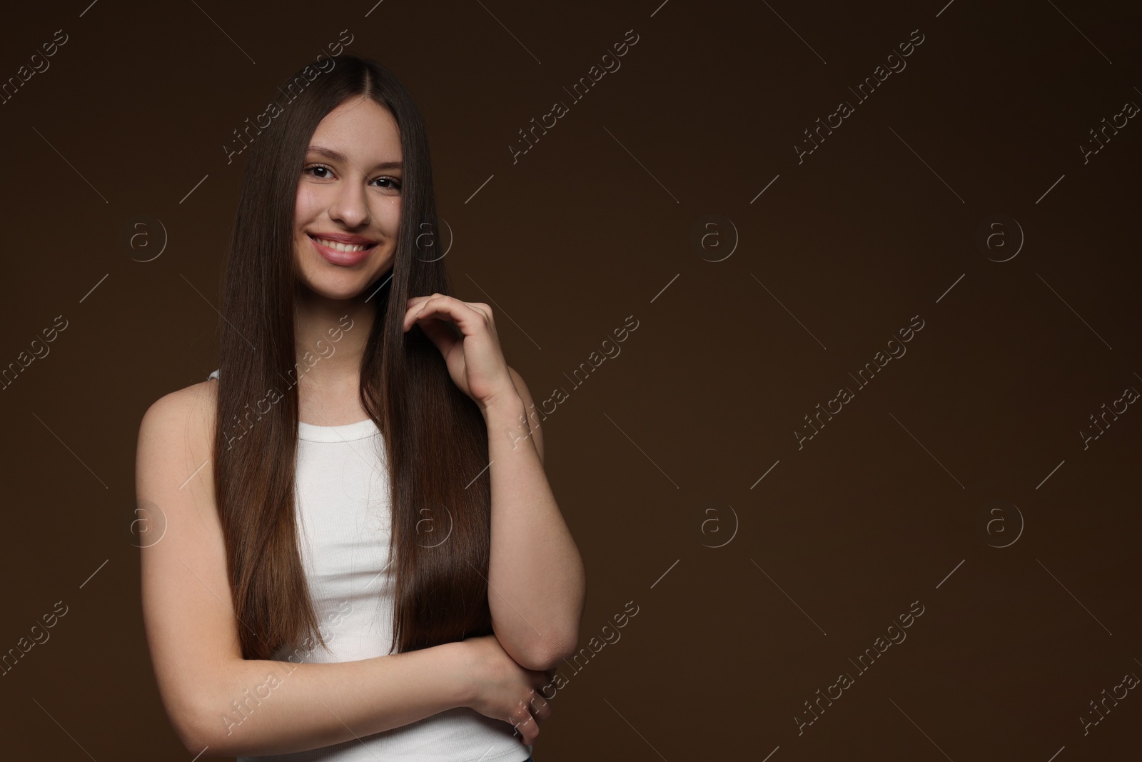 Portrait of smiling teenage girl with healthy long hair on brown background. Space for text Photo of Portrait of smiling teenage girl with healthy long hair on brown background. Space for text