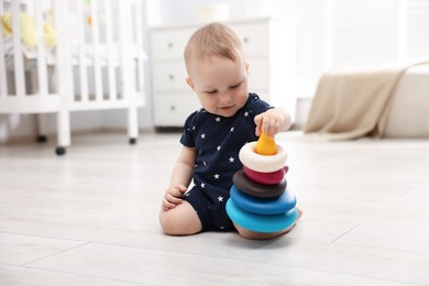 Photo of Cute little baby playing with toy pyramid in room