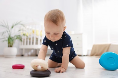 Photo of Cute little baby playing with toy pyramid in room