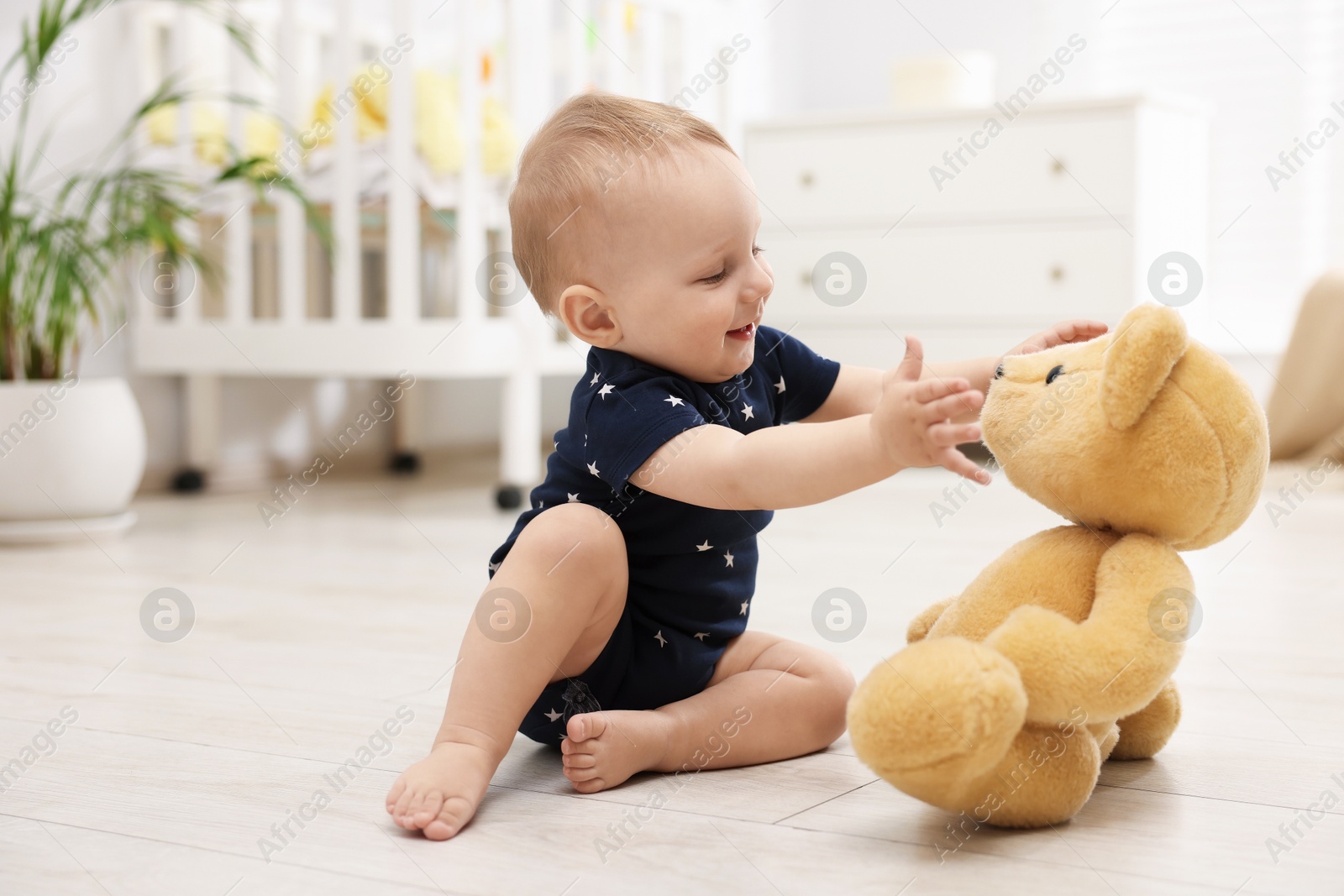 Cute little baby playing with teddy bear in room Photo of Cute little baby playing with teddy bear in room