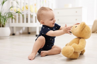 Photo of Cute little baby playing with teddy bear in room