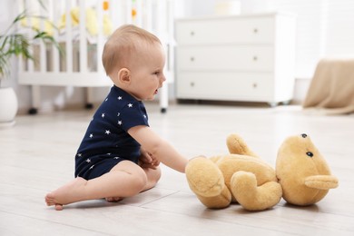 Photo of Cute little baby playing with teddy bear in room