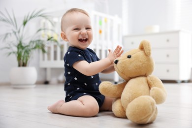 Photo of Cute little baby playing with teddy bear in room