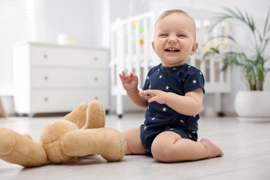 Photo of Cute little baby playing with teddy bear in room