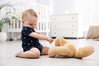 Photo of Cute little baby playing with teddy bear in room