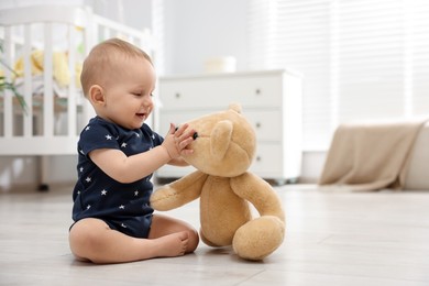 Photo of Cute little baby playing with teddy bear in room, space for text