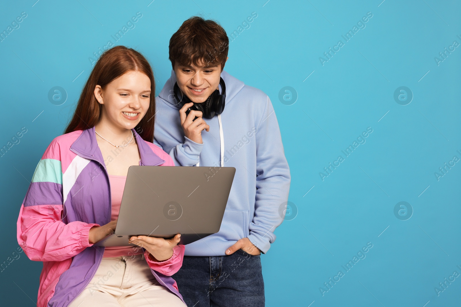 Teenage girl and boy with laptop on light blue background. Space for text Photo of Teenage girl and boy with laptop on light blue background. Space for text
