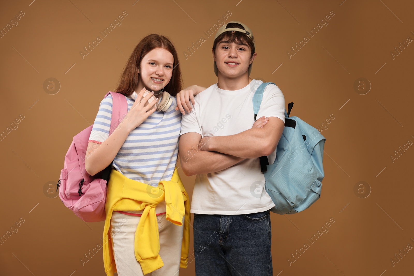 Teenage girl and boy with backpacks on brown background Photo of Teenage girl and boy with backpacks on brown background