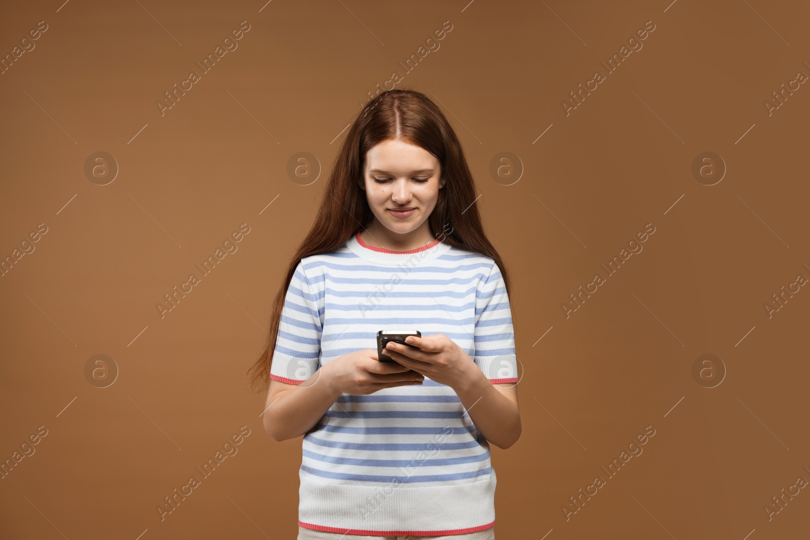Teenage girl with smartphone on brown background Photo of Teenage girl with smartphone on brown background