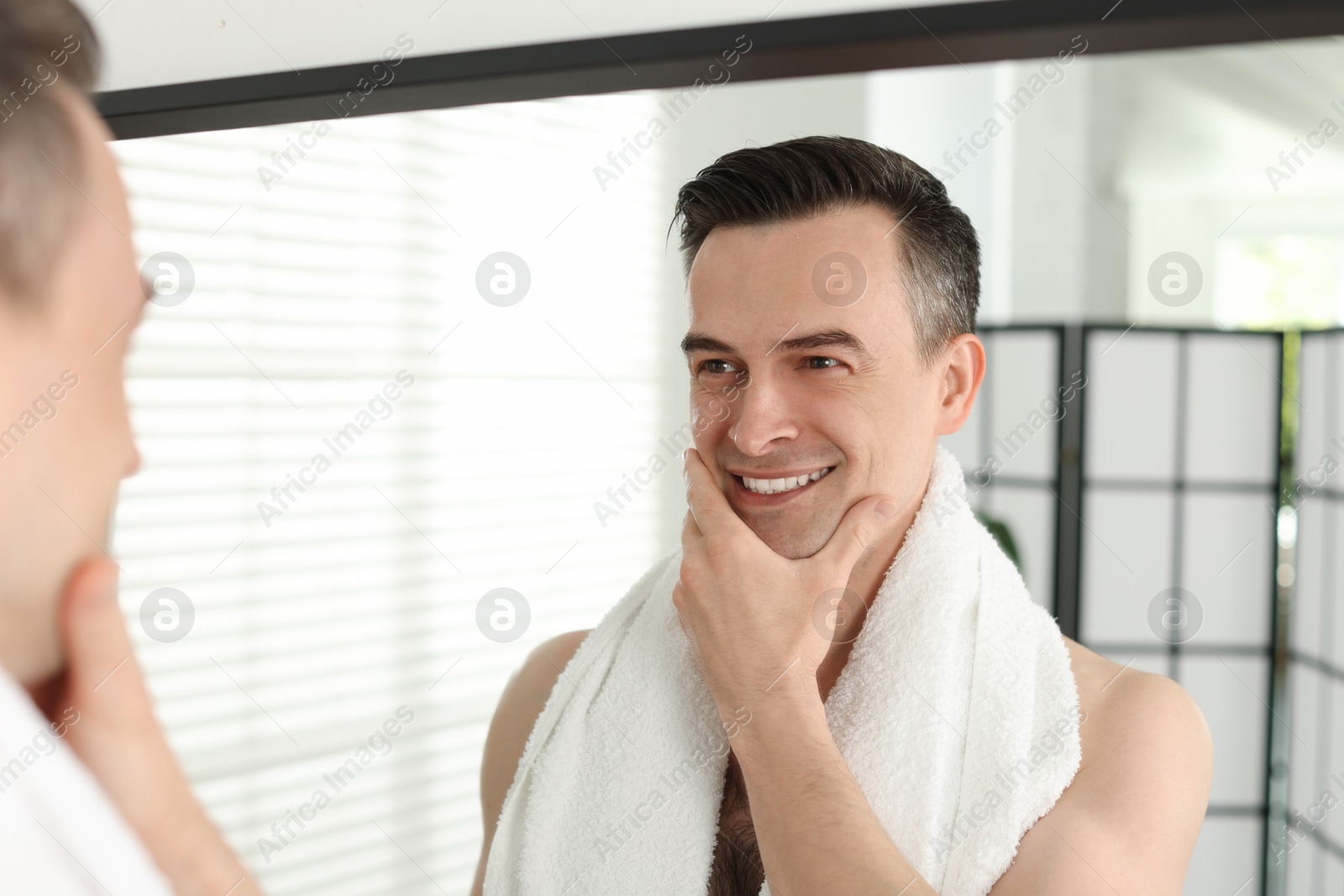 Smiling man after shaving looking at mirror in bathroom Photo of Smiling man after shaving looking at mirror in bathroom